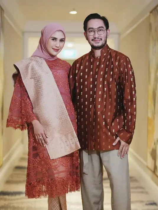 Baju kurung yang dibuat oleh Didiet Maulana dipadukan selendang dan bawahan kain songket warna coral. Jeje sang suami mengenakan atasan lengan panjang coklat bermotif. [@syahnazs]