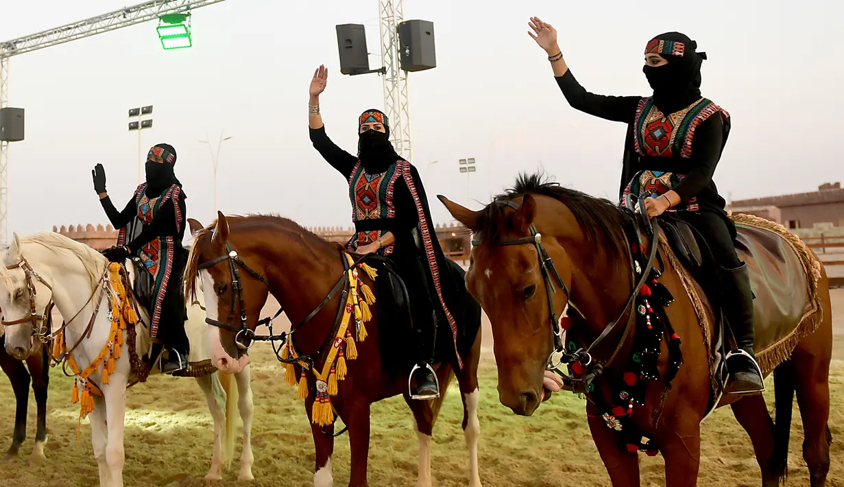 Perempuan Arab melambaikan tangan saat menunggangi kuda dalam Festival Souk Okaz 2019 di Kota Taif, Arab Saudi, Rabu (7/8/2019). Festival Souq Okaz merupakan ajang untuk berbagi warisan budaya dan sosial. (AMER HILABI/AFP)