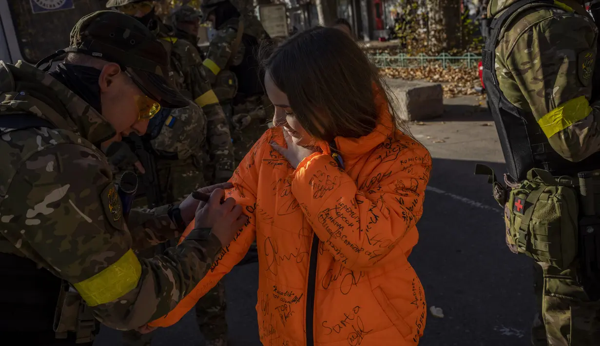 Seorang anggota pasukan pertahanan Ukraina menandatangani jaket milik seorang penduduk di Kherson, Ukraina selatan, Senin (14/11/2022). Perebutan kembali Kherson adalah salah satu keberhasilan terbesar Ukraina dalam hampir sembilan bulan sejak invasi Moskow. (AP Photo/Bernat Armangue)