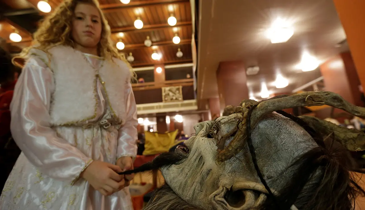 Seorang gadis berpakaian seperti malaikat sedang melihat topeng setan saat persiapan persiapan perayaan Krampus, di kota Bohemian selatan Kaplice, Republik Ceko (10/12). (Reuters/David W Cerny)