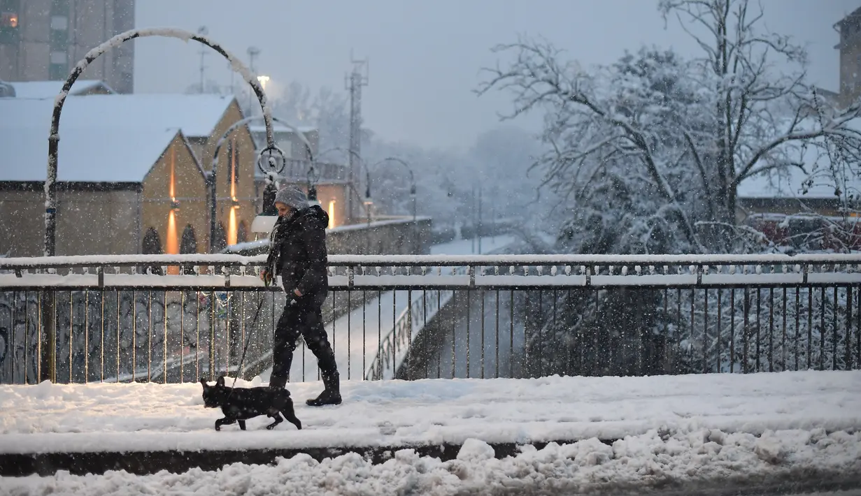 Seorang wanita berjalan-jalan dengan seekor anjing di tengah salju di Milan, Italia (28/12/2020). Hujan salju mengguyur Milan pada Senin (28/12). (Xinhua/Daniele Mascolo)