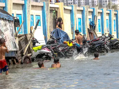 Sejumlah anak bermain genangan air banjir rob di kawasan akses pintu masuk menuju pelabuhan Kali Adem, Muara Angke, Jakarta, Senin (2/1). (Liputan6.com/Faizal Fanani)