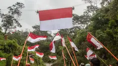 Personel Badan Pencarian dan Pertolongan Nasional (Basarnas) memasang bendera Merah Putih yang digantung pada tali yang membentang di atas sungai di Watu Kemloso, Yogyakarta, pada 13 Agustus 2025, menjelang peringatan ke-80 Hari Kemerdekaan Indonesia. (DEVI RAHMAN/AFP)