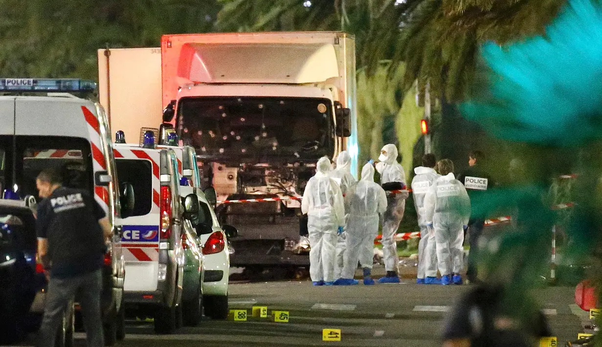 Polisi dan ahli forensik berdiri disamping sebuah truk yang menabrak kerumunan orang yang tengah menyaksikan festival di Nice, Prancis, Kamis (14/7). Sedikitnya 60 orang tewas dan ratusan lainnya luka akibat hantaman truk tersebut. (REUTERS/Eric Gaillard)