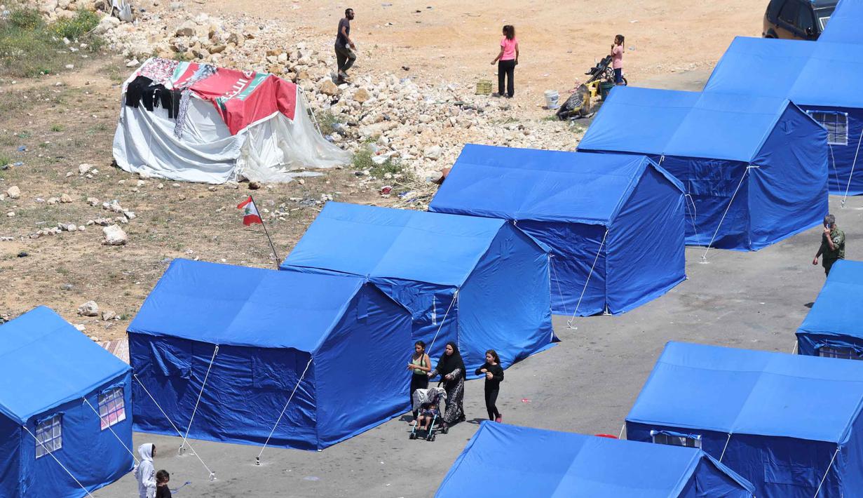 Warga Lebanon yang mengungsi berjalan di antara tenda-tenda biru yang didirikan pemerintah untuk orang-orang yang meninggalkan rumah dan desa mereka di pinggiran selatan Beirut dan Lebanon Selatan, Jumat 22 Mei 2026. (Anwar AMRO/AFP)