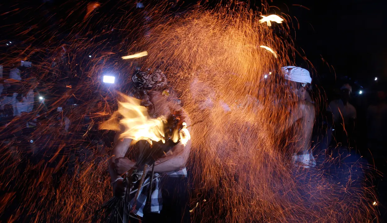 Ekspresi seorang pria bali saat dipukul dengan daun kelapa yang menyala dalam ritual Lukat Gni di Klungkung, Bali (16/3). Penyucian itu untuk membersihkan dari segala kotoran atau mala dengan sarana api. (AP Photo / Firdia Lisnawati)