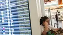 Seorang wanita beristirahat di samping papan informasi penerbangan di Terminal Internasional Bandara Haneda setelah penerbangan dibatalkan atau ditunda karena badai tropis Jangmi di Tokyo, Jepang, Rabu 3 Juni 2026. (Andrew CAALLERO-REYNOLDS/AFP)
