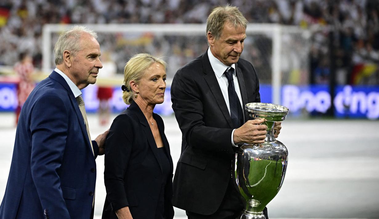 Istri mendiang legenda sepak bola Jerman, Franz Beckenbauer, Heidi Beckenbauer (tengah), mantan pesepak bola Jerman Bernard Dietz (Kiri), dan mantan kiper Timnas Jerman, Jurgen Klinsmann (kanan) membawa trofi Euro 2024 pada upacara pembukaan Euro 2024 di Allianz Arena, Munchen, Jerman, Sabtu (15/06/2024) WIB. (AFP/Tobias Schwarz)