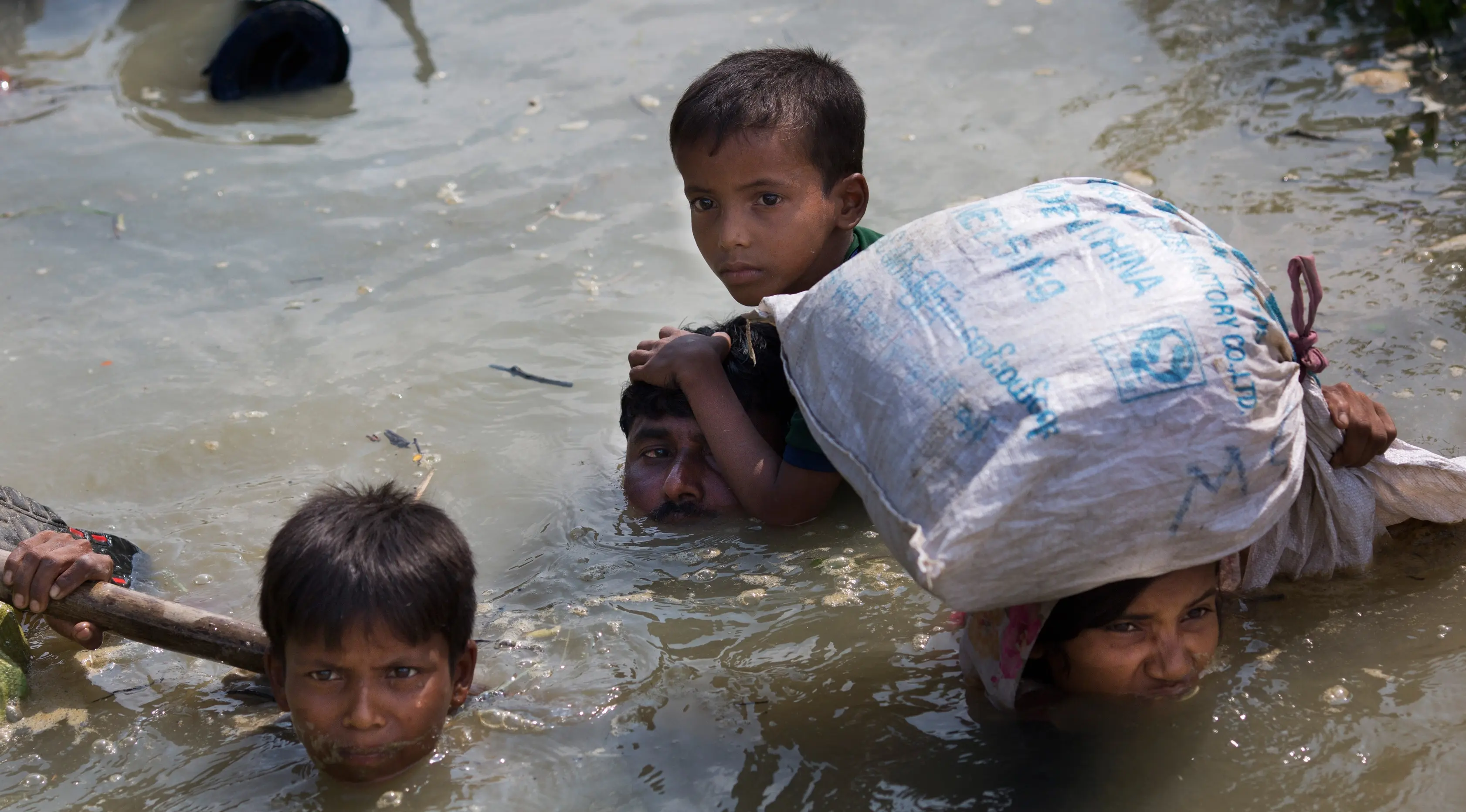Keluarga minoritas Rohingya membawa anak-anak mereka berjalan menyusuri sungai Naf untuk melarikan diri dari Myanmar menuju perbatasan Bangladesh, di daerah Teknaf Cox Bazar, 5 September 2017. (AP Photo/Bernat Armangue)