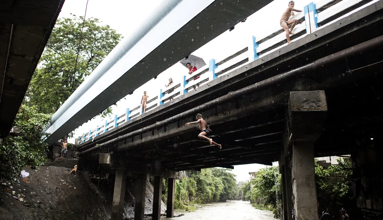 Seoarang bocah laki-laki melompat dari jembatan ke sungai saat ia bermain di sungai dengan arus yang sangat deras akibat hujan lebat di bawah jembatan di Manila, Filipina (11/6). (AFP Photo/Noel Celis)