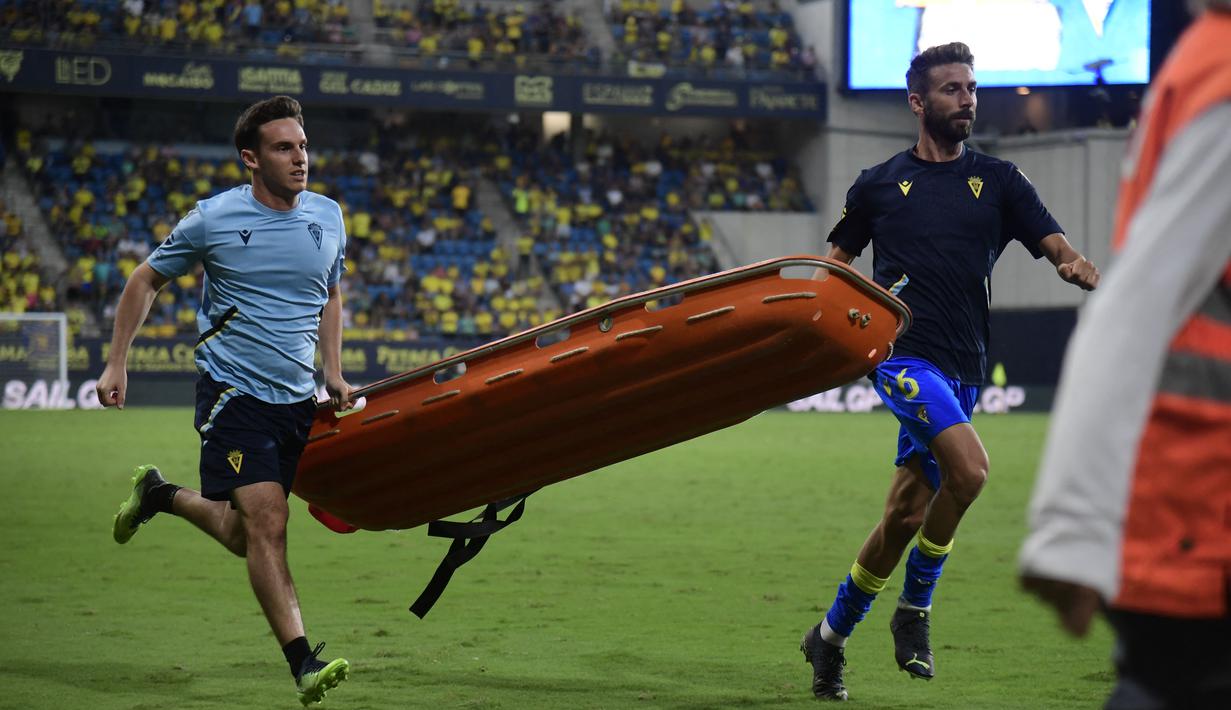 Petugas ofisial dari Cadiz juga sigap membawakan tandu untuk diberikan kepada petugas medis agar suporter yang mengalami insiden darurat medis bisa dibawa keluar stadion dan diberikan penanganan yang cepat. (AFP/Cristina Quicler)