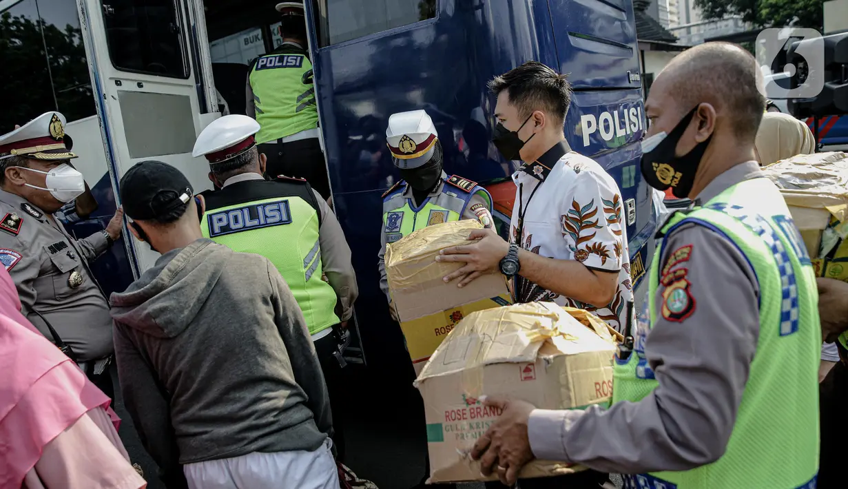 Polisi membantu membawakan barang penumpang yang terjaring razia travel gelap Ditlantas Polda Metro Jaya saat akan dipulangkan ke daerah asalnya, Jakarta, Kamis (29/4/2021). Sebanyak 115 kendaraan travel gelap diamankan. (Liputan6.com/Faizal Fanani)