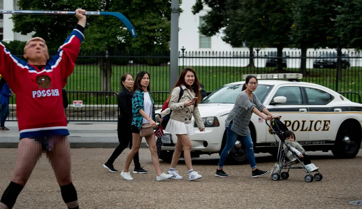 Wisatawan melihat seorang pria mengenakan topeng Presiden AS Donald Trump dan kostum tim hoki Rusia saat unjuk rasa di luar Gedung Putih di Pennsylvania Avenue di Washington, DC, (29/10). (AFP Photo/Brendan Smialowski)