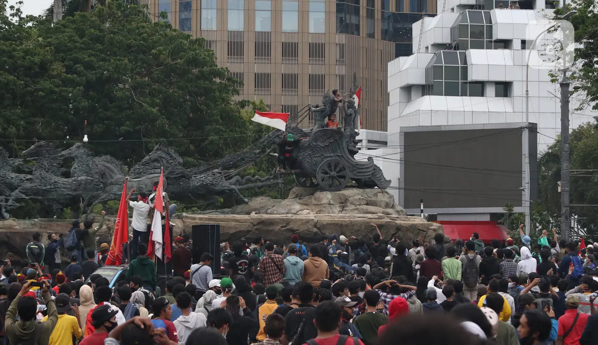 Massa aksi demo tolak omnibus law UU Cipta Kerja naik ke atas patung arjuna wiwaha mengibarkan bendera merah putih di Jalan Medan Merdeka Barat, Jakarta Pusat, Selasa (20/10/2020). Aksi mereka lantas disambut meriah oleh para massa yang masih bertahan. (Liputan6.com/Herman Zakharia)
