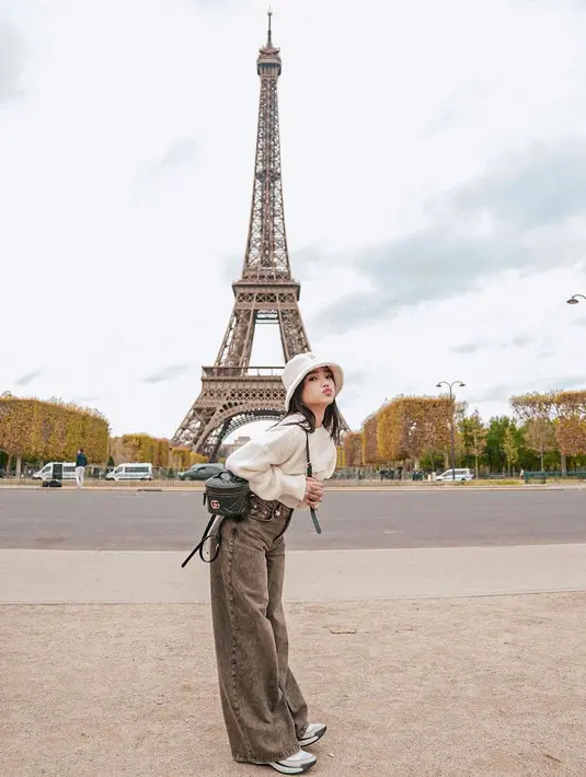 OOTD gemas dari Fuji dengan latar Menara Eiffel. Ia mengenakan tank top putih ditumpuknya dengan cropped sweater, dan wide-leg jeans abu-abu. Penampilannya semakin manis dengan padu padan sneakers dan bucket hat. [Foto: Instagram/fuji_an]