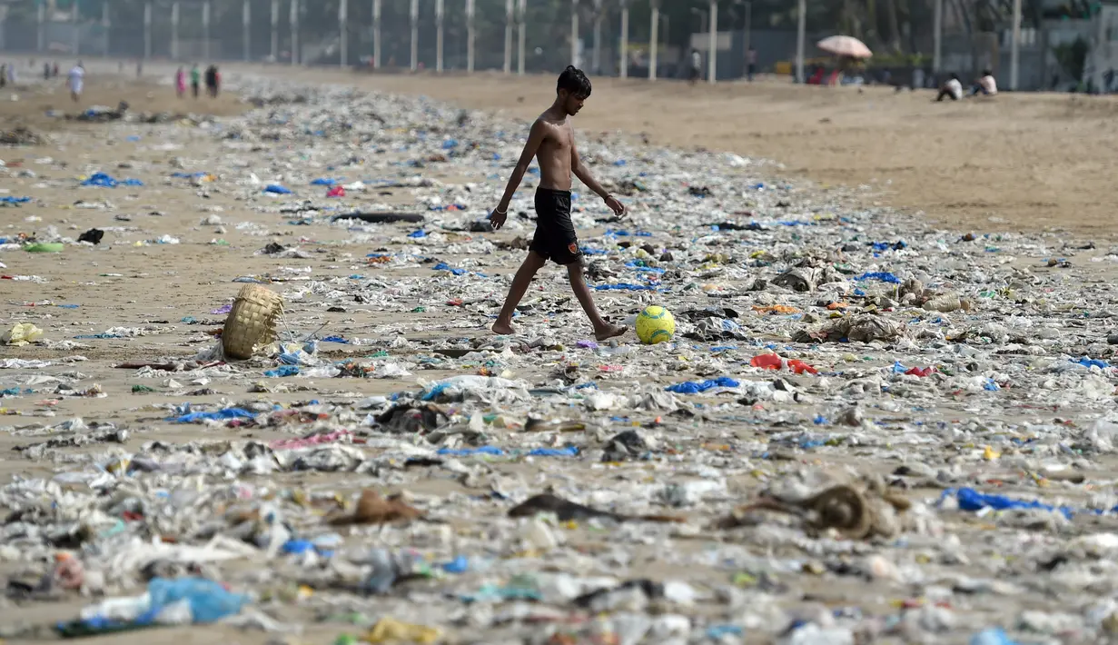 Seorang pria berjalan mengiring bola di pantai Juhu yang dipenuhi sampah plastik di Mumbai, India (2/6). (AFP PHoto/Punit Paranjpe)