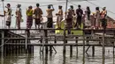 Sebagian besar warga mengungsi meninggalkan rumah mereka karena rusak berat dan tenggelam. Tampak dalam foto, para model lokal yang mengenakan pakaian tradisional menunggu untuk menyeberangi jembatan yang menghubungkan rumah-rumah yang sebagian terendam air laut akibat banjir pasang di desa Timbulsloko, Demak, Jawa Tengah pada Sabtu 18 April 2026. (DEVI RAHMAN/AFP)