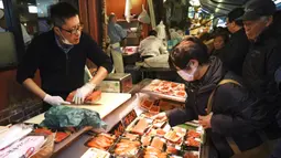 Pedagang melayani pembeli yang sedang mencari bahan-bahan untuk membuat makanan tahun baru atau osechi di Pasar Tsukiji, Tokyo, Jepang, Kamis (26/12/2019). Osechi harus dimasak hingga betul-betul kering agar tahan lama. (AP Photo/Eugene Hoshiko)