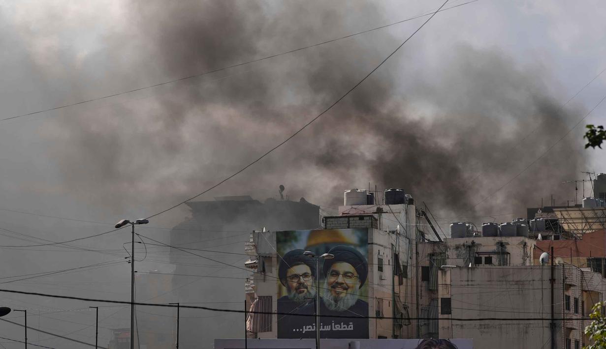 Serangan tersebut menyebabkan kerusakan signifikan pada bangunan apartemen pemukiman warga dan menimbulkan kepulan asap tebal. Tampak dalam foto, kepulan asap terlihat di balik potret mendiang pemimpin Hizbullah, Hassan Nasrallah (kanan) dan sepupunya, Hashem Safieddine, setelah serangan udara Israel di Dahiyeh, pinggiran selatan Beirut, Lebanon, Senin, 30 Maret 2026. (AP Photo/Hassan Ammar)