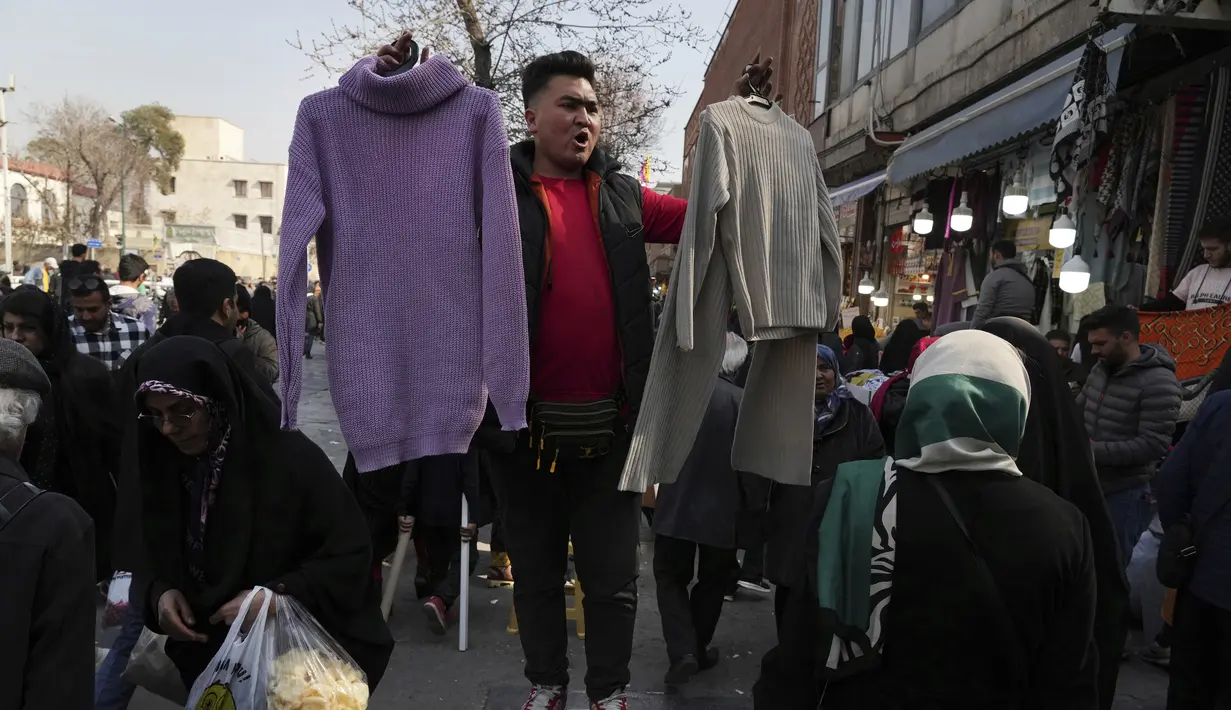 Seorang pramuniaga mengangkat pakaian perempuan untuk dijual di bazaar bersejarah tua Teheran, Iran, Minggu (26/2/2023). Inflasi pada bulan Januari lalu mencapai 53,4%. Menurut Pusat Statistik Iran, angka inflasi ini memburuk dibanding dua tahun lalu yang mencapai 41,4%. (AP Photo/Vahid Salemi)
