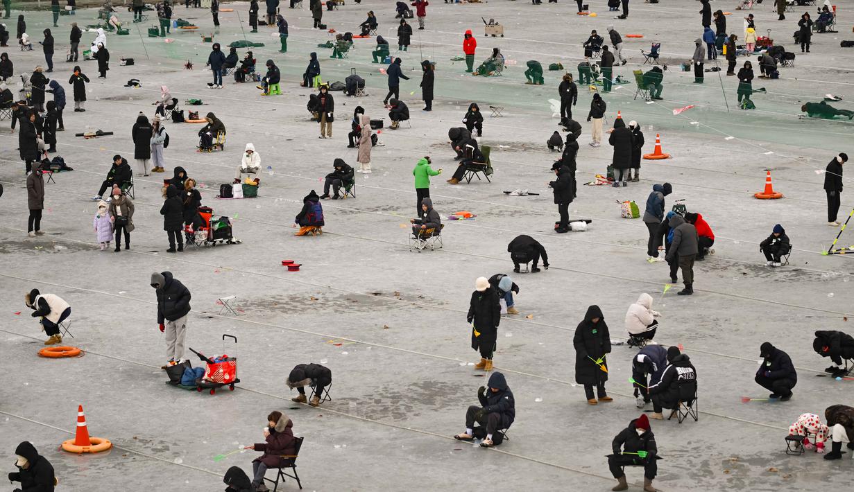 Mereka memenuhi area sungai Hwacheoncheon yang membeku sejak pagi hari untuk memancing ikan trout gunung (sancheoneo) melalui lubang di atas es sedalam 30 cm. Tampak dalam foto, orang-orang memancing melalui lubang-lubang di sungai yang membeku selama festival tahunan memancing di atas es, Hwacheon, Korea Selatan, pada Sabtu 10 Januari 2026. (Shin Yong-ju/AFP)