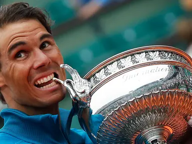 Petenis Spanyol, Rafael Nadal menggigit pialanya setelah mengalahkan Dominic Thien dari Austria pada partai final Prancis Terbuka di Stadion Roland Garros, Minggu (10/6). Ini merupakan trofi ke-11 Prancis Terbuka yang diraih Nadal. (AP/Michel Euler)