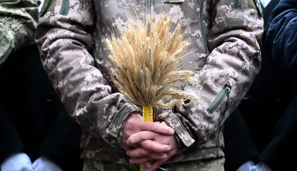 Seorang tentara Ukraina memegang hiasan tradisional Natal 'Didukh' saat ikut serta dalam prosesi Malam Natal di Lviv pada 24 Desember 2025. Di tengah ancaman invasi Rusia, warga Ukraina bersukacita menyambut perayaan Natal 2025. (YURIY DYACHYSHYN/AFP)
