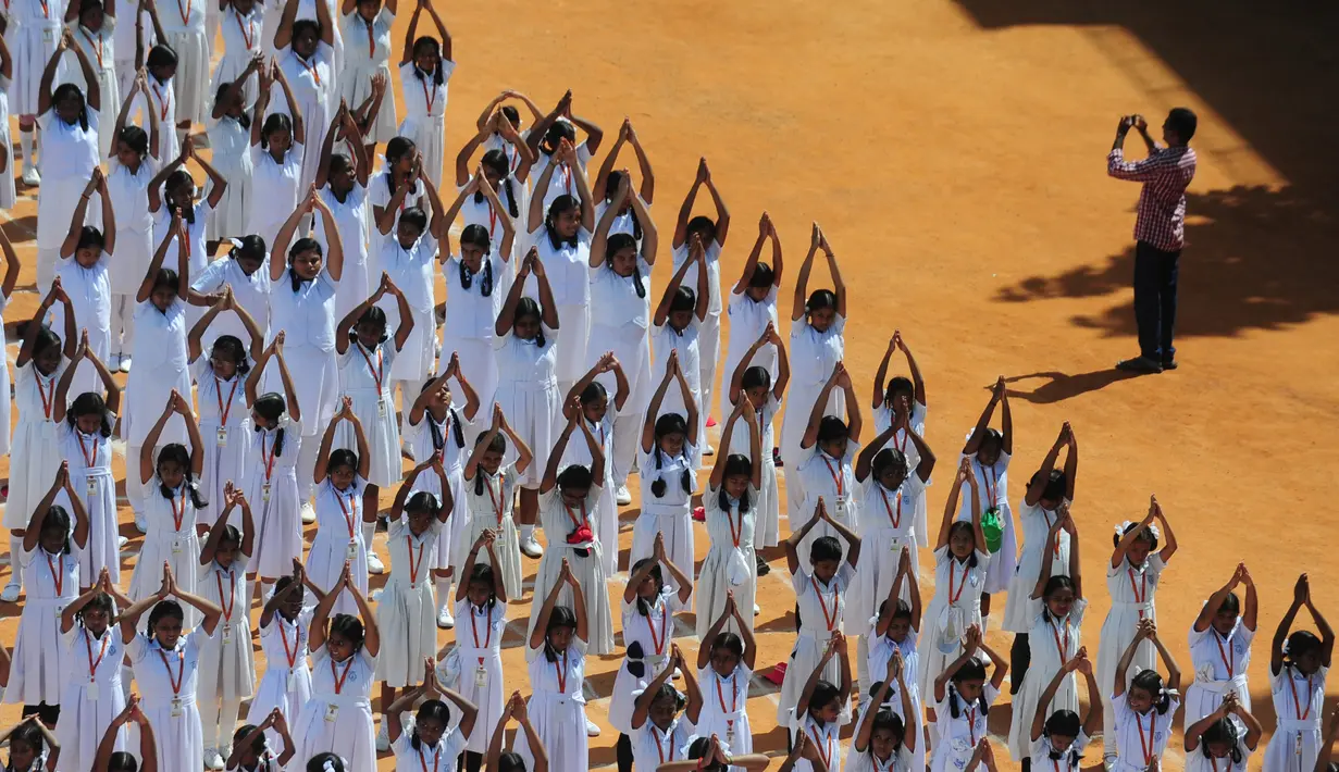 Seseorang mengabadikan momen saat Ribuan pelajar India melakukan senam yoga di Chennai, India, Senin (20/6). Kegiatan ini untuk memeriahkan perayaan Hari Yoga Internasional. (AFP PHOTO/ Arun Sankar)