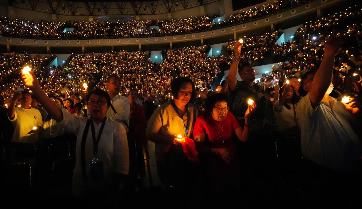 Sekitar 16.000 jemaat dari wilayah Jabodetabek memadati arena untuk mengikuti ibadah tersebut. Tampak dalam foto, orang-orang memegang lilin elektrik sambil bernyanyi selama kebaktian Malam Natal di Indonesia Arena, Kompleks Gelora Bung Karno, Jakarta, Rabu 24 Desember 2025. (AP Photo/Tatan Syuflana)