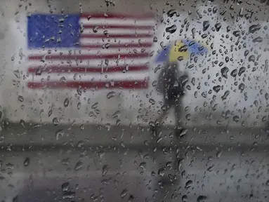 Seorang pejalan kaki membawa payung sambil berjalan melewati lukisan bendera Amerika di San Francisco, Rabu (11/1/2023). California yang dilanda badai berjuang untuk membersihkan dan memperbaiki kerusakan yang meluas. (AP Photo/Jeff Chiu)