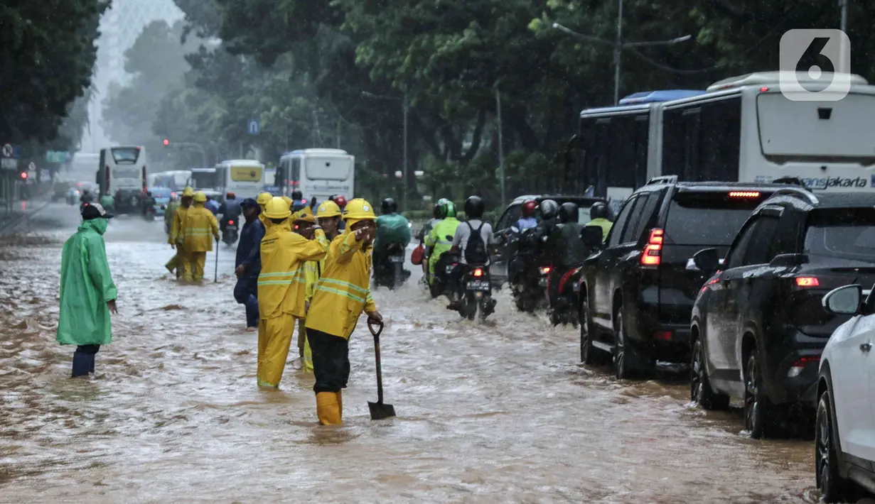 Petugas mengatur lalu lintas saat air menggenangi Jalan Medan Merdeka Barat, Jakarta, Kamis (24/1/2020). Hujan deras yang mengguyur Jakarta sejak pagi tadi mengakibatkan genangan air di Jalan Medan Merdeka Barat. (Liputan6.com/Faizal Fanani)