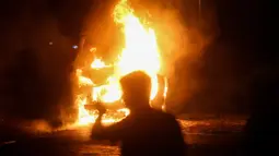 Seseorang melewati kendaraan polisi yang terbakar setelah ribuan pengunjuk rasa marah dengan pemberlakuan kembali jam malam Covid-19 pada akhir pekan di depan gedung Majelis Nasional di Beograd, Selasa (7/7/2020). Mereka mengecam cara pemerintah mengatasi pandemi Covid-19. (OLIVER BUNIC/AFP)