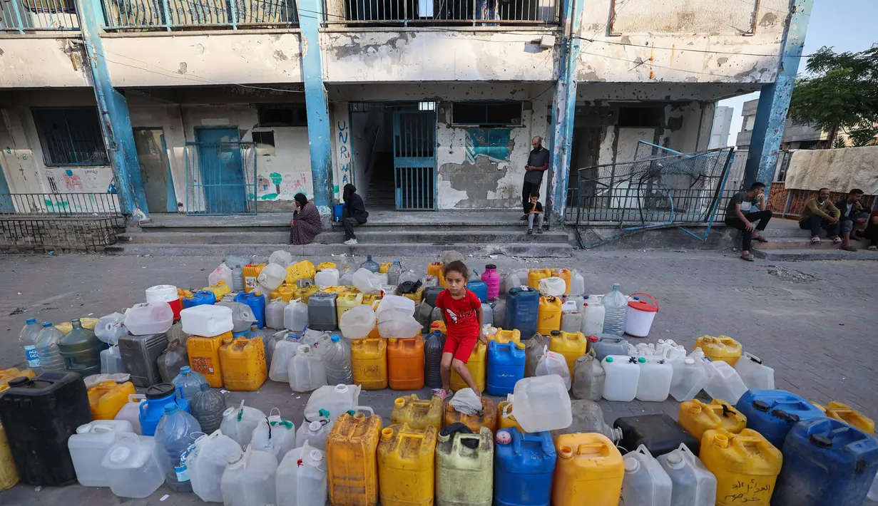 Seorang anak perempuan Palestina duduk di atas jerigen kosong sambil menunggu truk distribusi air di sekolah Abou Helou yang dikelola UNRWA, tempat para pengungsi perempuan berlindung di kamp pengungsi Bureij di Jalur Gaza tengah, pada 17 Juli 2025. (Eyad BABA/AFP)