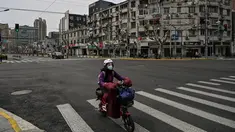 Seorang wanita mengendarai skuter di jalan yang sepi di distrik Yangpu, di Shanghai (28/3/2022). Jutaan orang di pusat keuangan China dikurung di rumah mereka pada Maret 28 ketika bagian timur Shanghai dikunci untuk mengekang wabah Covid terbesar di negara itu. (AFP/Hector Retamal)
