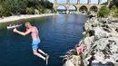 Seorang pria melompat ke sungai di dekat Pont du Gard atau Jembatan Gard di Vers-Pont-du-Gard, Prancis, Rabu (21/8/2019). Pont du Gard merupakan bagian dari saluran air yang panjangnya hampir 50 km. (Pascal GUYOT/AFP)