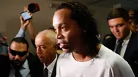 Mantan pemain timnas Brasil, Ronaldinho dikawal oleh polisi meninggalkan kantor pengadilan di Asuncion, ibu kota Paraguay, Jumat (6/3/2020). Ronaldinho bersama saudara laki-lakinya berurusan dengan pihak berwenang Paraguay karena menggunakan paspor palsu untuk memasuki negara itu. (AP/Jorge Saenz)