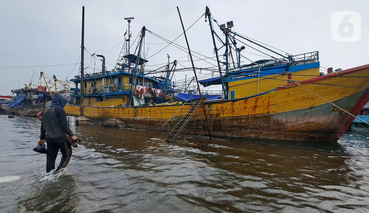 Nelayan melintasi banjir rob saat cuaca ekstrem di Pelabuhan Muara Baru, Penjaringan, Jakarta Utara, Rabu (28/12/2022). Banjir ROB, hujan deras dan  cuaca buruk melanda kawasan Pelabuhan Muara Baru saat siang menjelang sore hari. (Liputan6.com/Johan Tallo)