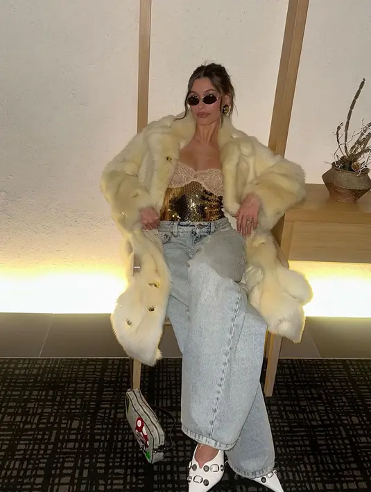 <p>Ia mengenakan coat bulu dengan panjang selutut dan baggy jeans. Melengkapi tampilannya yang glamor, Hailey menggunakan bustier sequin berwarna emas dan kacamata hitam sebagai aksesori. [Instagram/haileybieber]</p>