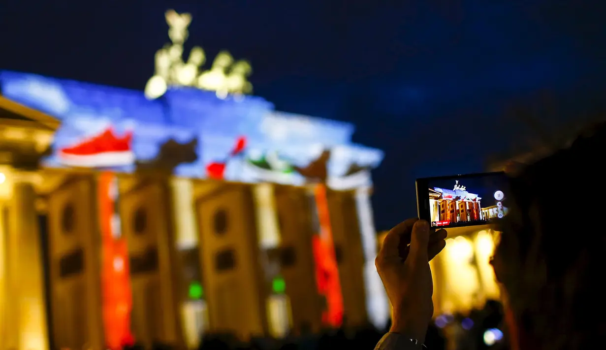 Seorang pria mengambil gambar Gerbang Brandenburg yang dihiasi cahaya saat pembukaan Festival cahaya, Jerman, Sabtu (10/10/2015). Festival ini merupakan event tahunan yang diadakan setiap bulan Oktober selama dua belas hari.(REUTERS/Hannibal Hanschke)
