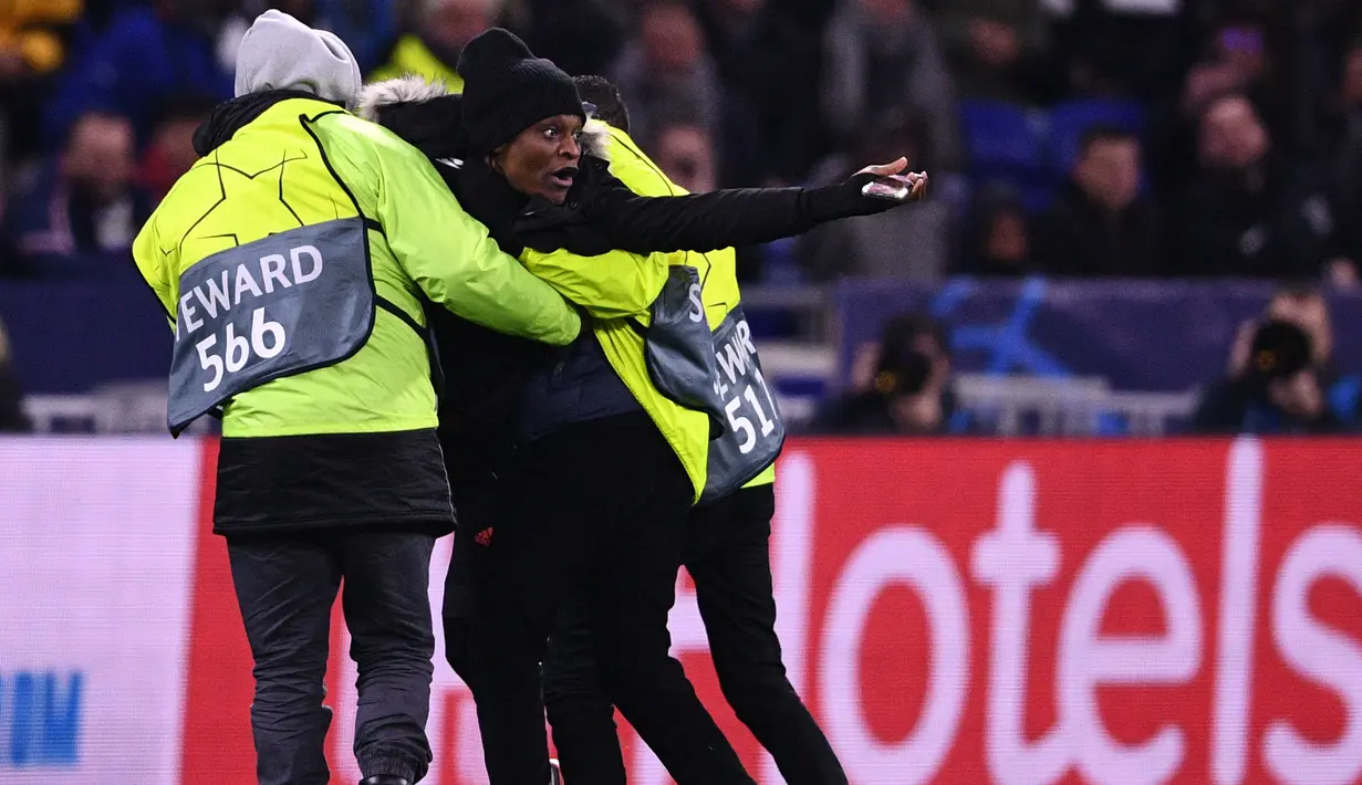 Petugas membawa seorang penggemar setelah menghampiri Cristiano Ronaldo selama pertandingan antara Lyon dan Juventus pada leg pertama babak 16 Liga Champions di Stadion Olimpiade Lyon di Decines, Prancis (26/2/2020). Dalam pertandingan ini Lyon berhasil mengalahkan Juventus 1-0. (AFP/Franck Fife)