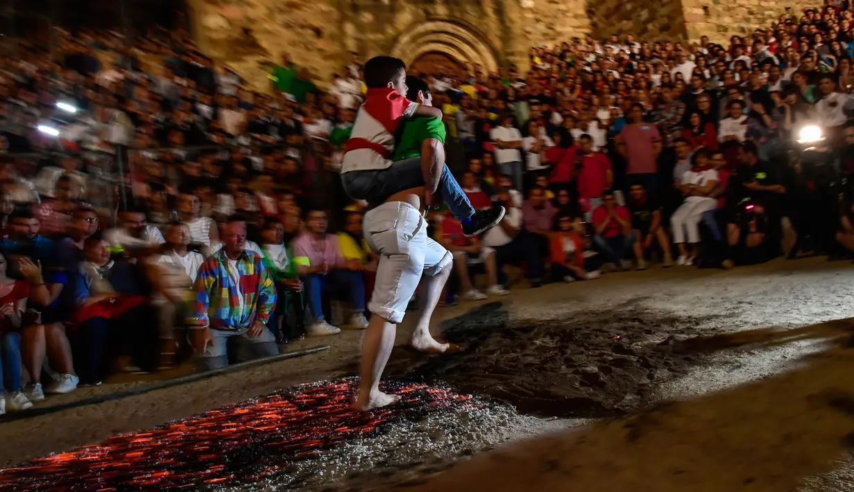 Seorang pria membawa anak lelaki di punggungnya sambil berjalan di atas bara api selama malam San Juan di San Pedro Manrique, Spanyol Utara, Minggu (24/6). Tradisi kuno Spanyol ini diperingati untuk menyambut musim panas. (AP Photo/Alvaro Barrientos)