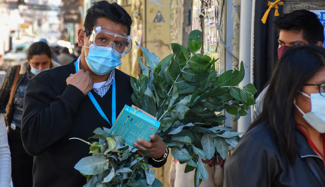 Seorang pria yang mengenakan masker membawa seikat ramuan obat tradisional yang digunakan untuk pengobatan penyakit pernapasan di Cochabamba, Bolivia pada 25 Juli 2020. Kasus infeksi virus corona dan kematian akibat COVID-19 semakin meningkat di negara Amerika Selatan tersebut. (AP Photo/Dico Solis)