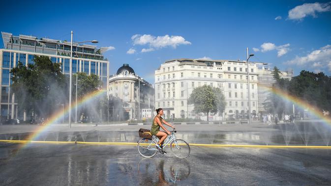 Seorang pesepeda melewati semprotan air di Schwarzenbergplatz di Wina, Austria (28/7/2020). Suhu tertinggi di Wina mencapai angka 37,2 derajat Celsius pada Selasa (28/7). (Xinhua/Guo Chen)
