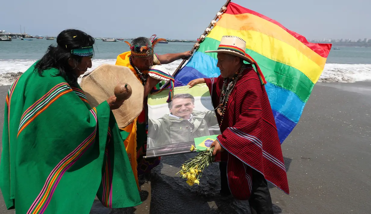 Dukun Peru memegang poster Presiden Brasil Jair Bolsonaro selama ritual tahun baru  di pantai Agua Dulce, Lima, Kamis (27/12). Ritual dimaksudkan untuk membawa kekuatan dan energi ke seluruh dunia sehingga ada kedamaian dan ketenangan. (AP/Martin Mejia)