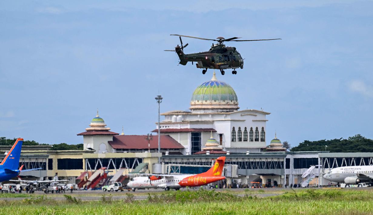 Pesawat dan helikopter dikerahkan secara intensif untuk distribusi logistik dan evakuasi, terutama ke daerah yang akses daratnya terputus. Tampak dalam foto, sebuah helikopter kembali ke pangkalan setelah mengirimkan bantuan kepada korban banjir, di Pangkalan Tentara Nasional Indonesia (TNI) Angkatan Udara (AU) di Blang Bintang, Provinsi Aceh, pada Minggu 7 Desember 2025. (Chaideer MAHYUDDIN/AFP)