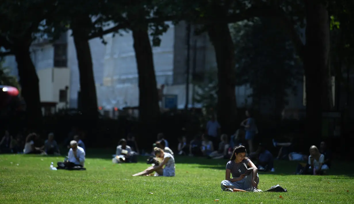 Seorang wanita membaca buku di bawah sinar matahari di Victoria Tower Gardens dekat Gedung Parlemen di London (23/7/2019). Suhu melonjak di atas 30C (86F) di Inggris pada 23 Juli dengan para peramal cuaca memperkirakan suhu setinggi 37C (96.8F) sebelum akhir pekan. (AFP Photo/Ben Stansall)