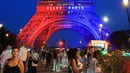 Orang-orang berjalan di bawah Menara Eiffel yang diterangi cahaya warna-warna khas, dengan pesan bertuliskan "Allez Paris" ("Ayo, Paris"), pada malam menjelang pertandingan final Liga Champions 2025/2026 antara Paris Saint-Germain (PSG) dan Arsenal, Kamis 29 Mei 2026. (Ludovic MARIN/AFP)