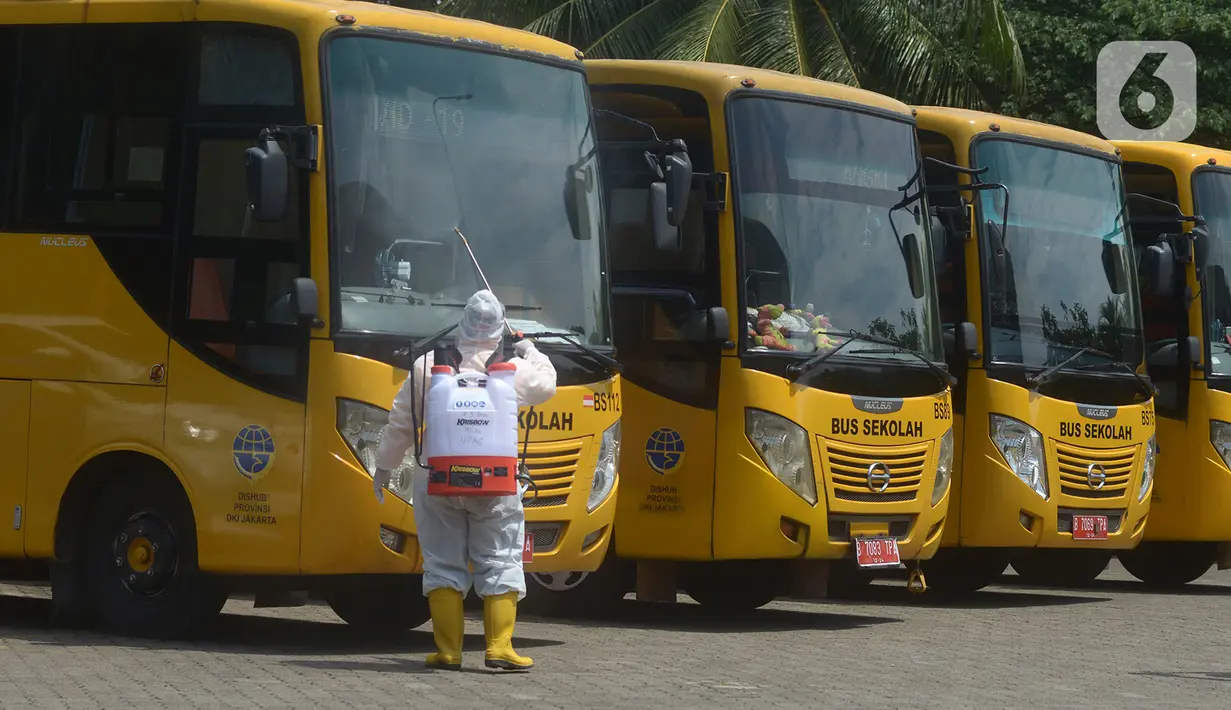 Petugas ber-APD menyemprotkan disinfektan pada bus sekolah di Posko Gabungan PSBB dan Gakplin Protkes, Puskesmas Jatinegara, Jakarta, (22/9/2020). Sejumlah unit bus sekolah kini dialihfungsikan menjadi kendaraan untuk mengantar pasien Covid-19 berstatus OTG menuju Wisma Atlet. (merdeka.com/Imam Buho