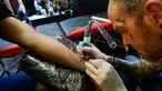 Seorang seniman tato membuat gambar lebah di pergelangan tangan seorang Mancunian di Manchester (28/5). Seniman ini membuat tato lebah untuk menggalang dana yang diberikan kepada korban serangan bom konser Ariana Grande. (AP Photo/Mstyslav Chernov)