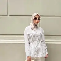 Citra Kirana tampil dengan atasan kemeja putih yang memiliki aksen dua kantong depan dengan kerutan dan kancing depan emas, dipadukan celana putih panjang dan kerudung motif warna beige. [@citraciki]